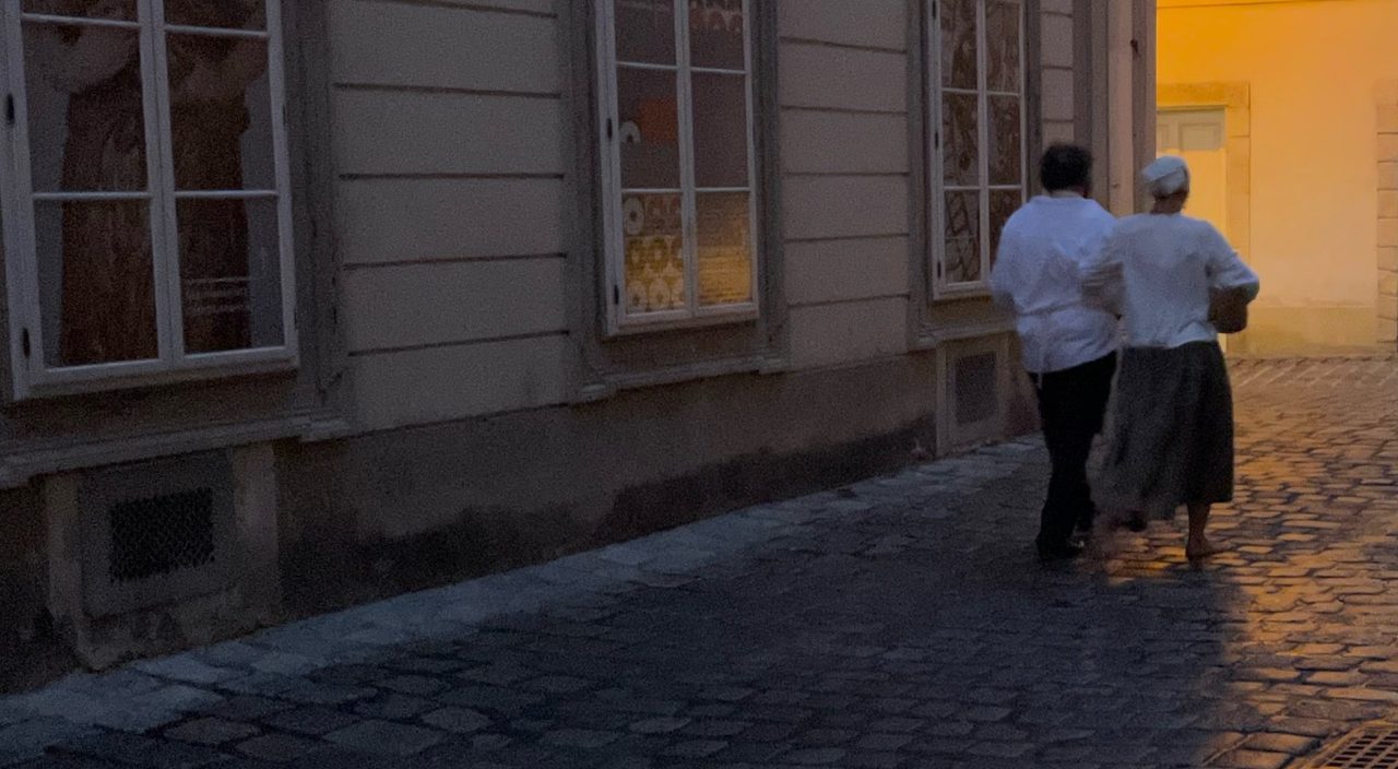 Zwei Figuren gehen am Abend durch eine Gasse der Wiener Altstadt