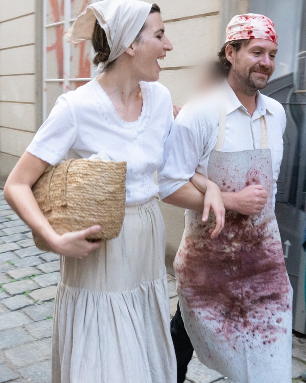 Zwei Figuren gehen Arm in Arm durch eine Gasse