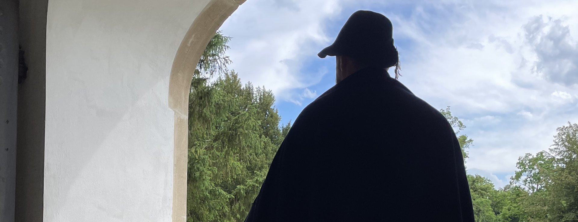 Eine Figur im langen Umhang steht in einem Torbogen